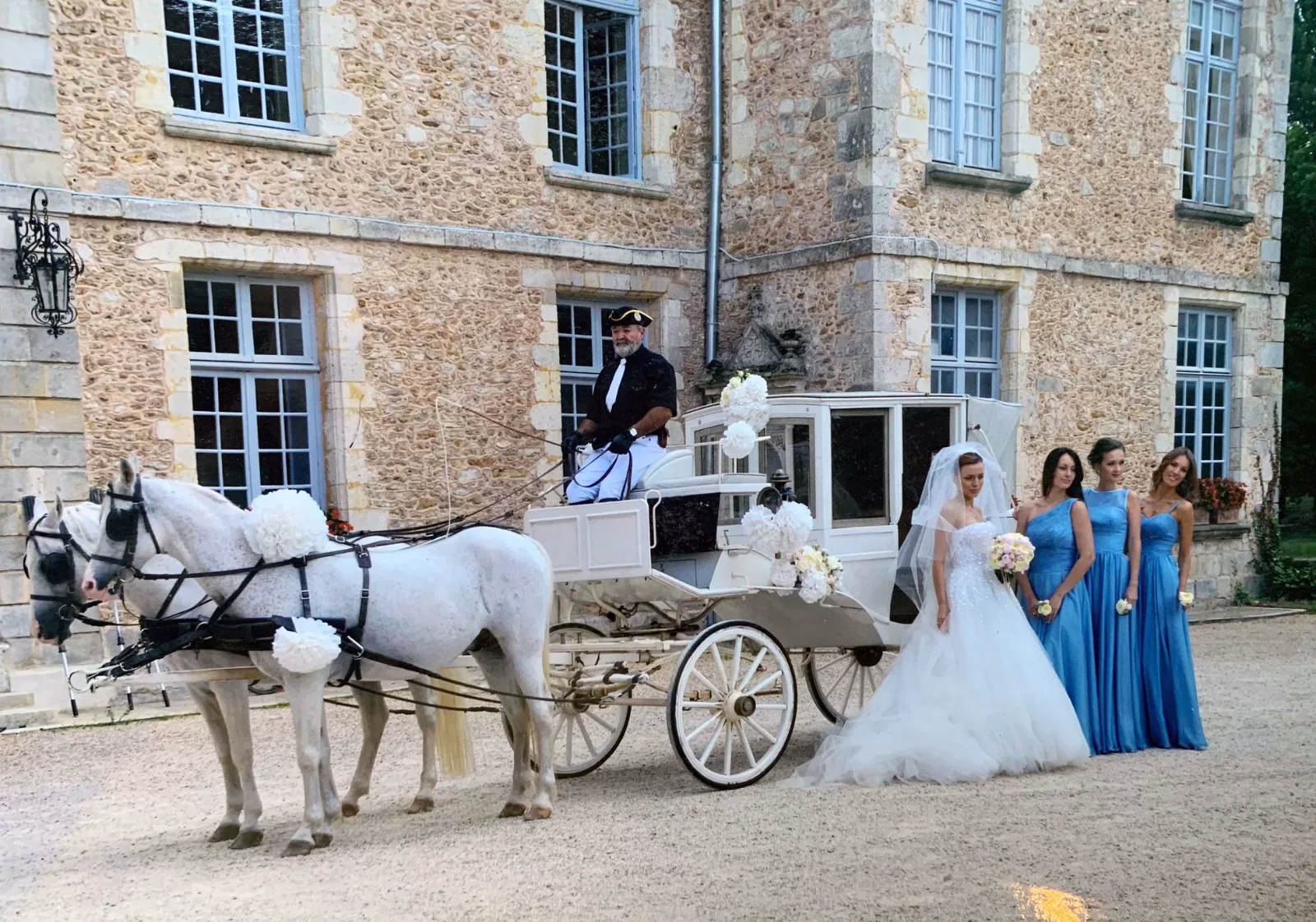 Mariée et demoiselles d'honneur en robes bleues devant la calèche fleurie d'un château