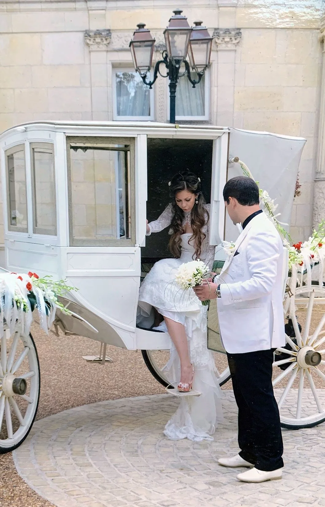La mariée descend d'une calèche fleurie, aidée par le groom