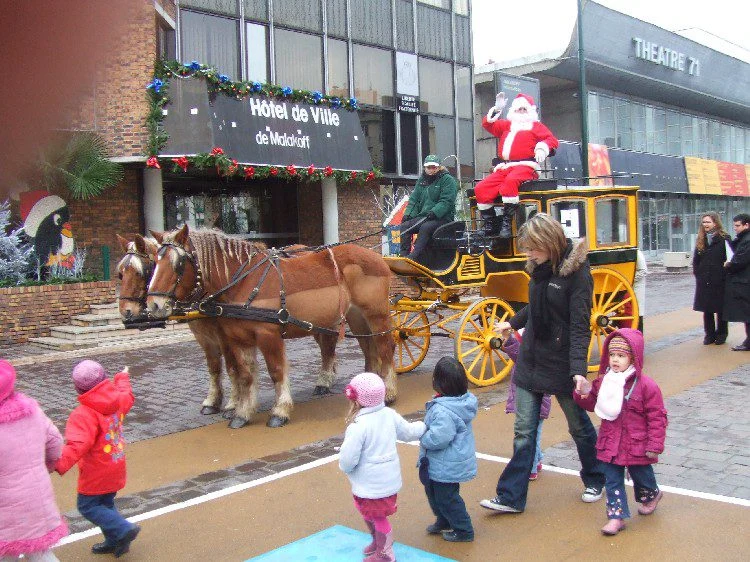 Diligence jaune et Père Noël devant un hôtel de ville, entourés d'enfants