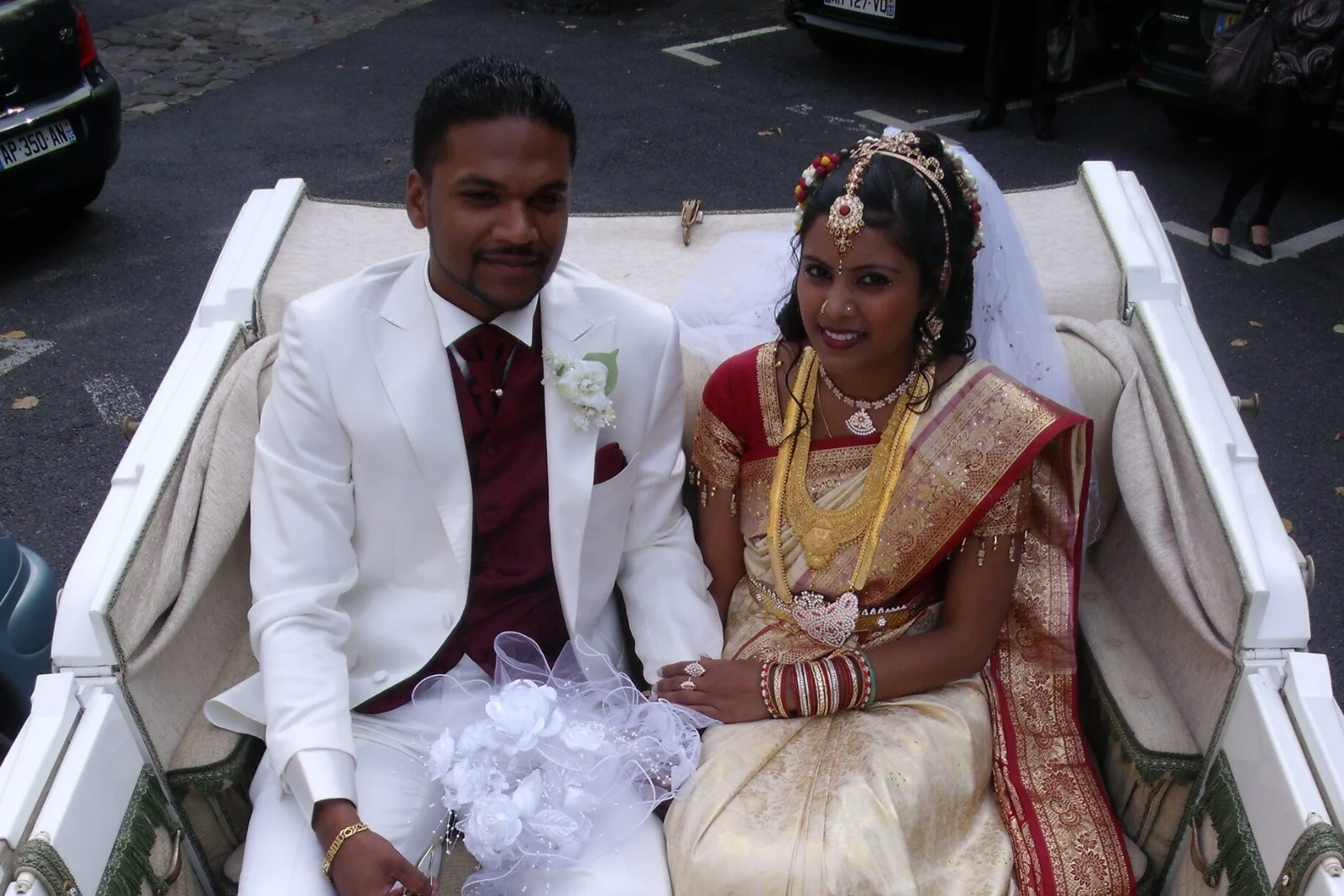Mariés de tradition indienne dans la calèche : la mariée en sari rouge et or et parures d'or, le marié en costume blanc
